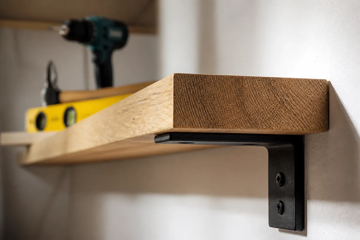 Détail d’une fixation d’étagère en bois avec équerre métallique sur un mur clair